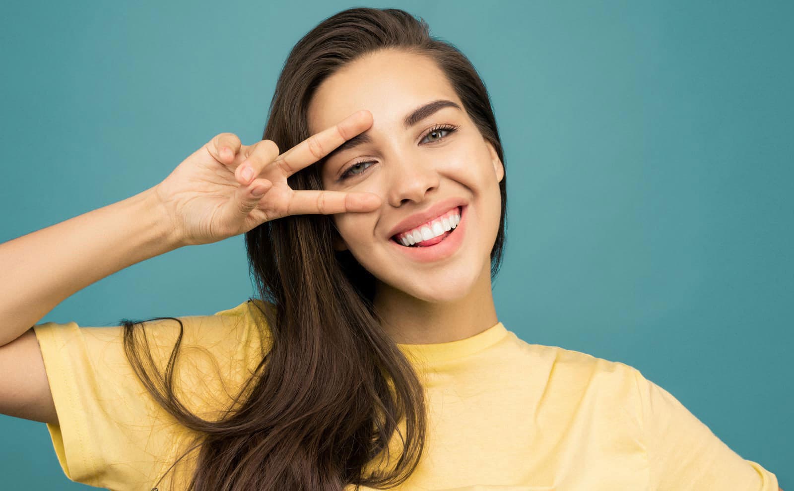 Ragazza che sorride facendo il segno della pace su sfondo azzurro
